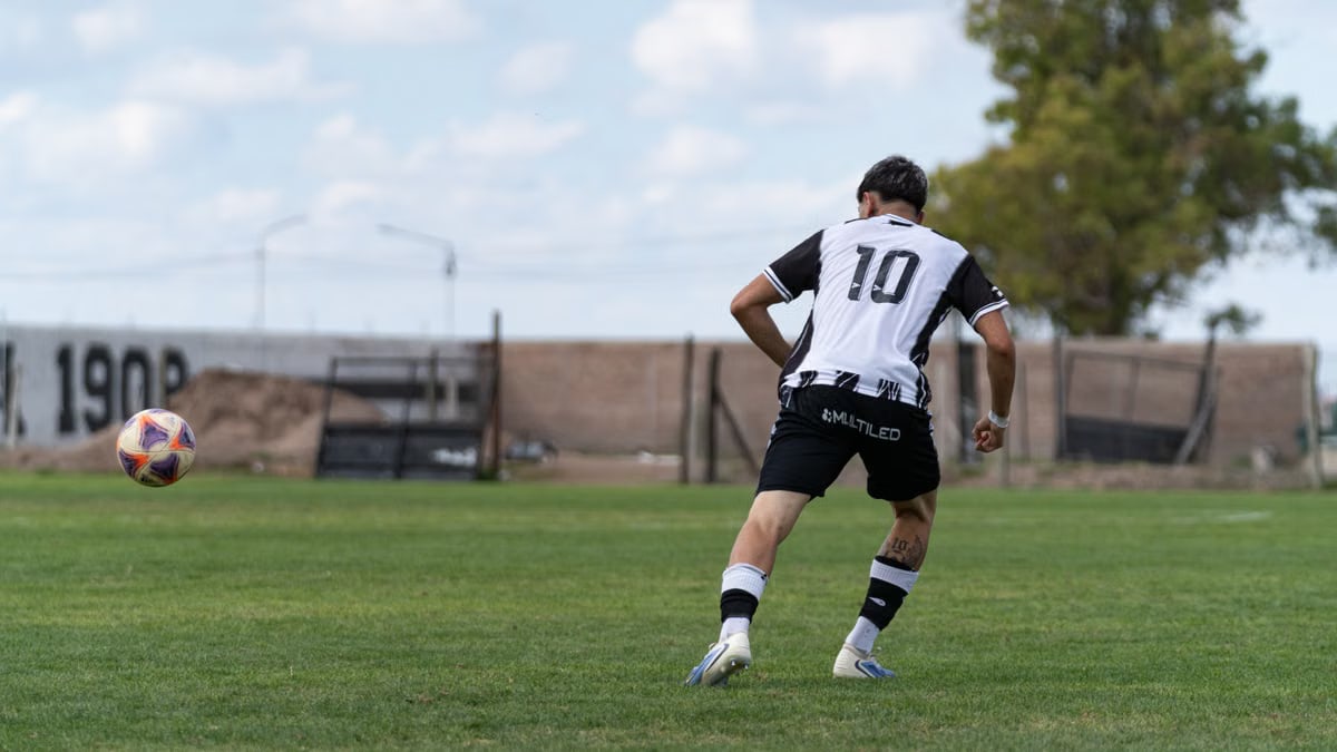 A young soccer player in a black and white jersey prepares to kick a soccer ball on a grassy field.